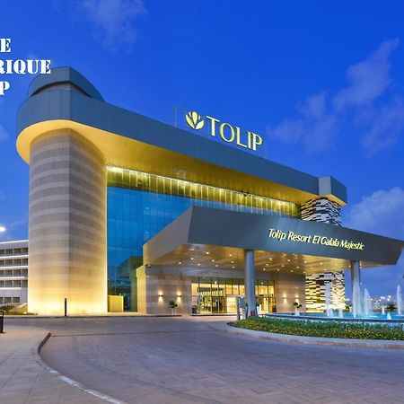 Tolip Resort El Galala Majestic Ain Sukhna Luaran gambar The photo shows a modern hotel building named "Tolip Resort & Spa," featuring a sleek architectural design with large glass windows. The hotel is illuminated against a twilight sky, showcasing its prominent signage. In the foreground, there is a well