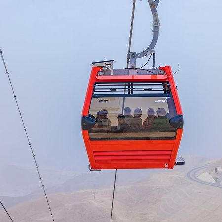Tolip Resort El Galala Majestic Ain Sukhna Luaran gambar The photo shows a red gondola lift suspended in the air, traveling along cables. Inside the gondola, a group of people can be seen. The background features a hazy landscape, possibly mountains or hills, indicating an elevated area. The scene conveys 