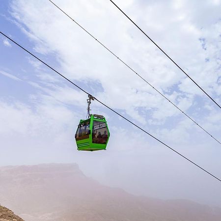 Tolip Resort El Galala Majestic Ain Sukhna Luaran gambar The photo shows a green cable car suspended in the air, traveling along overhead cables. The backdrop features a hazy landscape, likely mountainous or elevated terrain, with a cloudy sky. The scene suggests a scenic transportation method, possibly us