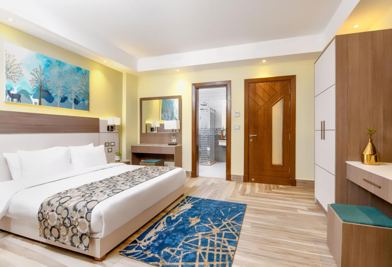 Tolip Resort El Galala Majestic Ain Sukhna Luaran gambar The photo shows a well-decorated hotel room. There is a large bed with white linens and a decorative throw blanket. The room features a wooden wardrobe and a bedside table with lamps. A colorful rug is placed on the floor, adding warmth to the space.