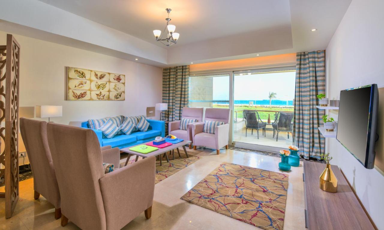 Tolip Resort El Galala Majestic Ain Sukhna Luaran gambar The photo shows a bright and modern living room. It features a blue sofa with decorative cushions, two light-colored armchairs, and a coffee table. A large area rug adds warmth to the space, which is decorated with a subtle pattern. The walls have so