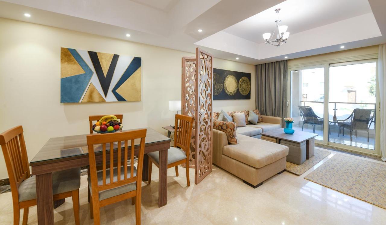 Tolip Resort El Galala Majestic Ain Sukhna Luaran gambar The photo shows a modern and stylish interior of a living space. It features a seating area with a plush sofa and decorative cushions, complemented by a wooden coffee table. There is a dining table with wooden chairs nearby. 

On the walls, there are