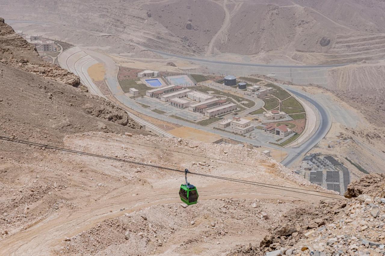 Tolip Resort El Galala Majestic Ain Sukhna Luaran gambar The photo shows a mountainous landscape with a steep, dry terrain. In the foreground, there is a green cable car or gondola traveling along a cable. Below, a complex of buildings and roads can be seen, likely part of a resort or recreational area. Th