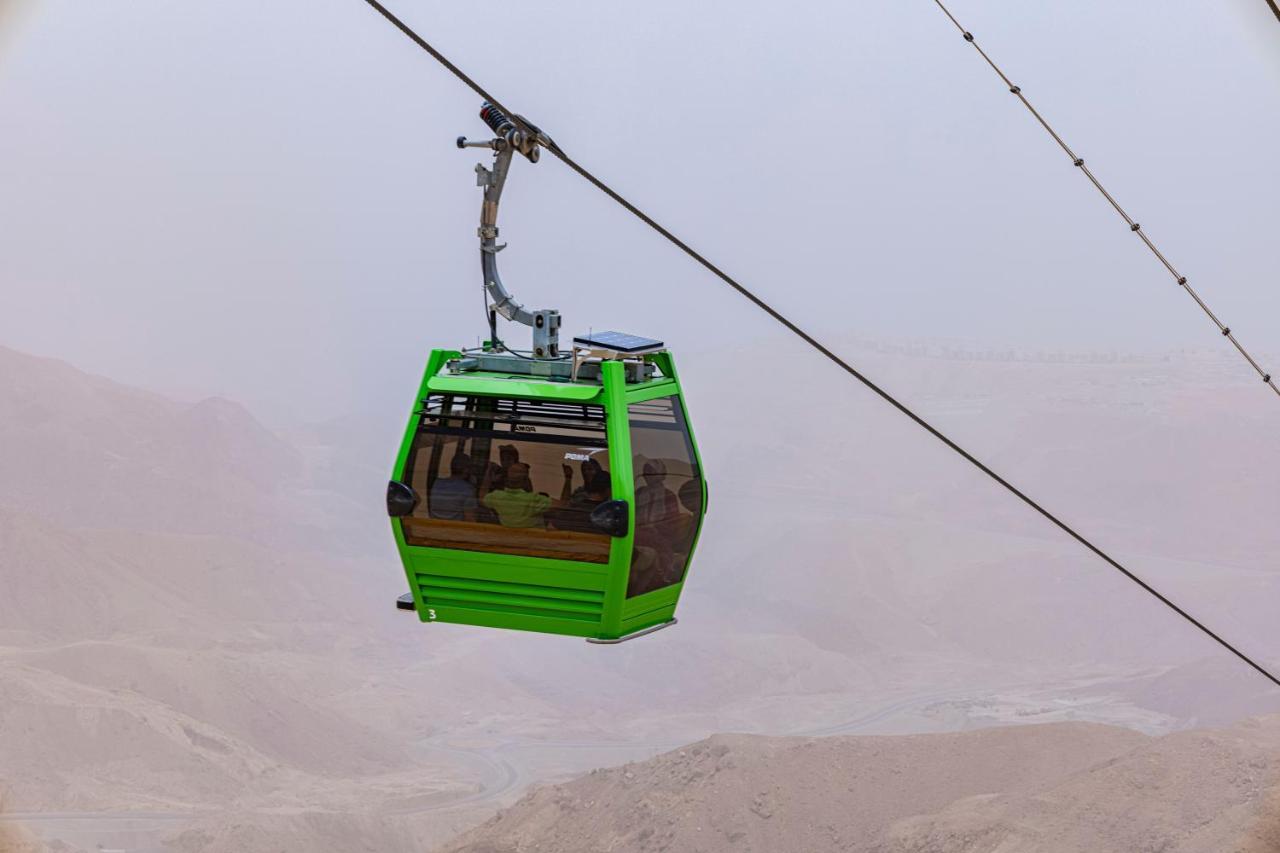 Tolip Resort El Galala Majestic Ain Sukhna Luaran gambar The photo shows a green cable car suspended in the air, moving along a wire. The cable car appears to be traversing a mountainous landscape, which looks rocky and arid. The surrounding environment is somewhat foggy or hazy, suggesting limited visibil