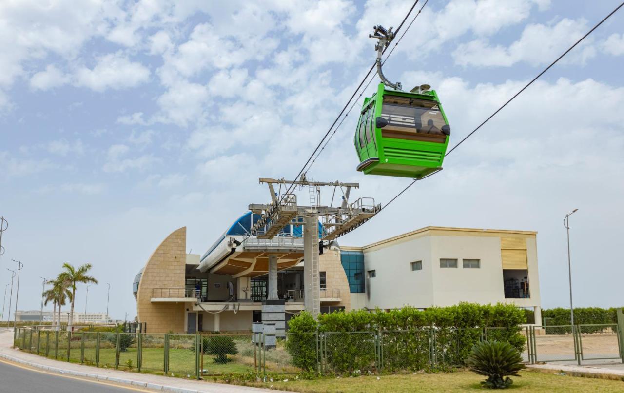 Tolip Resort El Galala Majestic Ain Sukhna Luaran gambar The photo shows a cable car or gondola system in operation, featuring a green-colored gondola. It is suspended from cables and moving towards a station, which appears to be a modern building with a unique architectural design. The station has large w