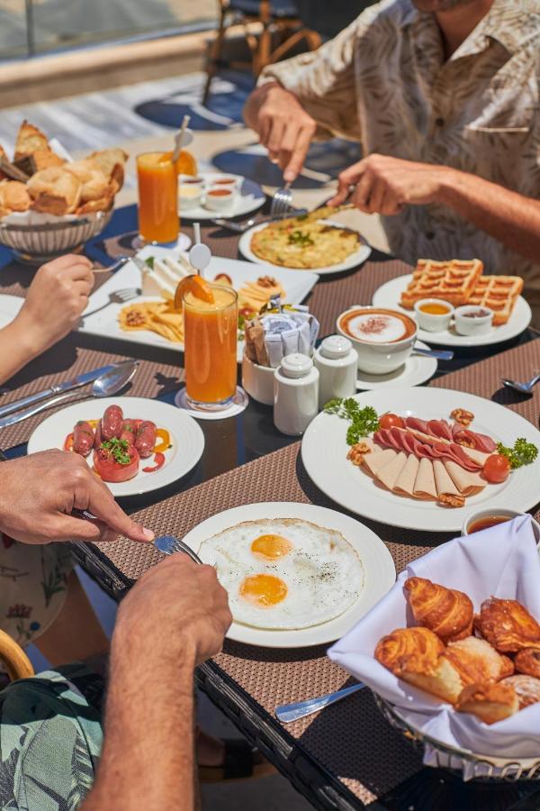 Tolip Resort El Galala Majestic Ain Sukhna Luaran gambar The photo features a spread of breakfast dishes on a table. There are two sunny-side-up eggs on one plate, surrounded by various food items, including slices of ham, sausages, and fresh tomatoes. Another plate holds a serving of waffles. A bowl with 