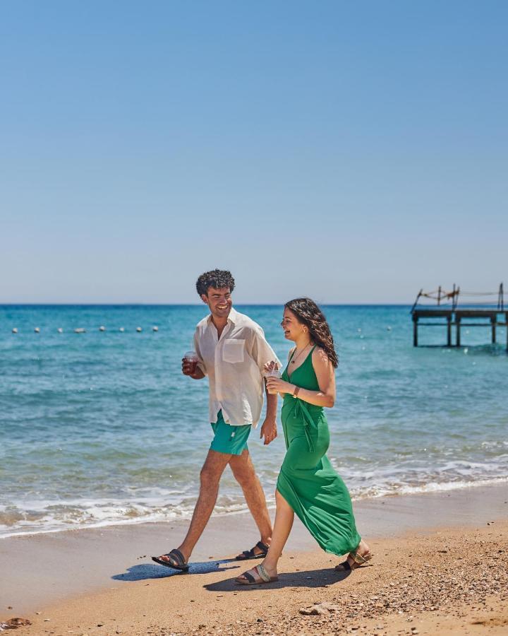 Tolip Resort El Galala Majestic Ain Sukhna Luaran gambar The photo shows a couple walking along a beach. The man is wearing a white short-sleeved shirt and green shorts, while the woman is dressed in a flowing green dress. They both appear to be enjoying the pleasant weather, with the ocean in the backgrou