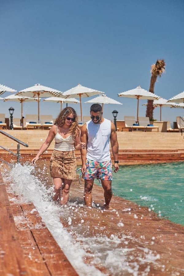 Tolip Resort El Galala Majestic Ain Sukhna Luaran gambar The photo depicts a couple walking along a poolside area. They are enjoying a sunny day near a swimming pool, with splashes of water around them. The woman is wearing a light-colored top and a patterned skirt, while the man is dressed in a sleeveless