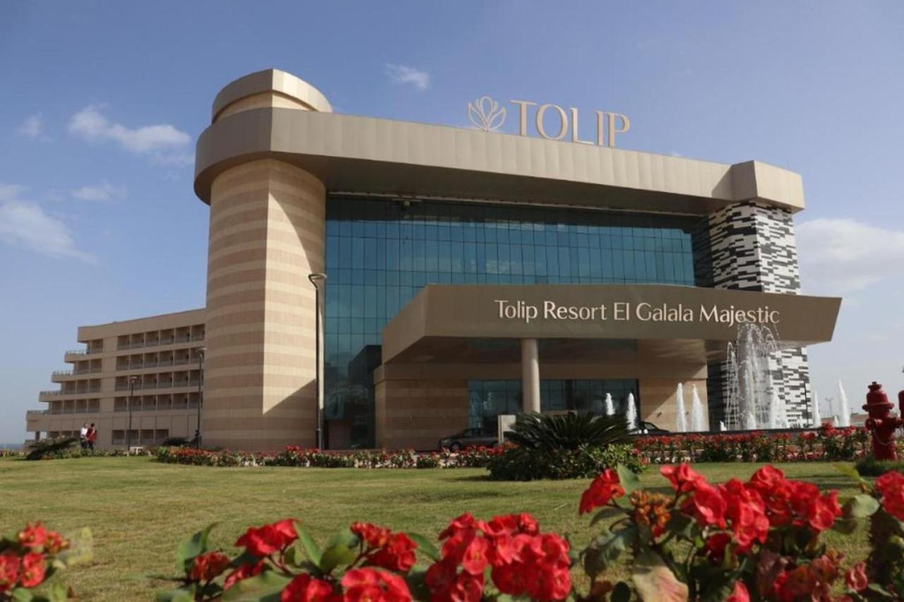 Tolip Resort El Galala Majestic Ain Sukhna Luaran gambar The photo shows a modern hotel building named "Tolip Resort El Galala Majestic." The structure features a distinctive architectural design with large glass windows and a prominent entrance. Surrounding the building are well-maintained lawns and vibra