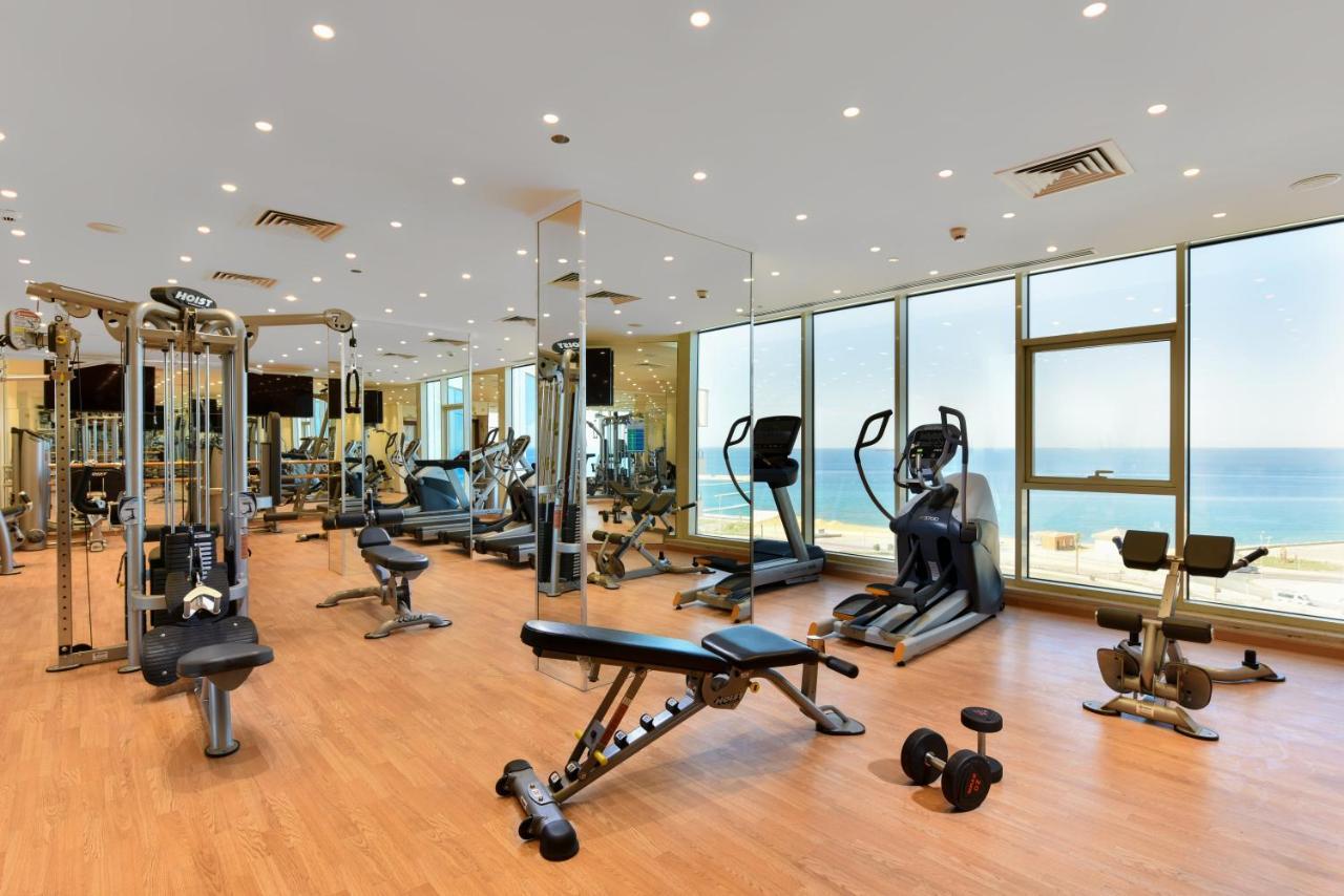 Tolip Resort El Galala Majestic Ain Sukhna Luaran gambar The photo shows a modern gym interior with a variety of fitness equipment. There are cardio machines like treadmills and ellipticals, along with strength training equipment such as free weights and benches. The gym features large windows that offer a