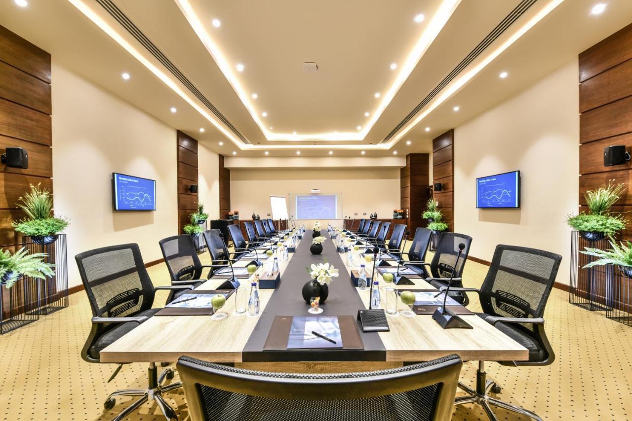 Tolip Resort El Galala Majestic Ain Sukhna Luaran gambar The photo shows a modern conference room designed for meetings. It features a long rectangular table at the center, surrounded by ergonomic black chairs. The room is well-lit with ceiling lights and has a neutral color scheme. There are two large scr