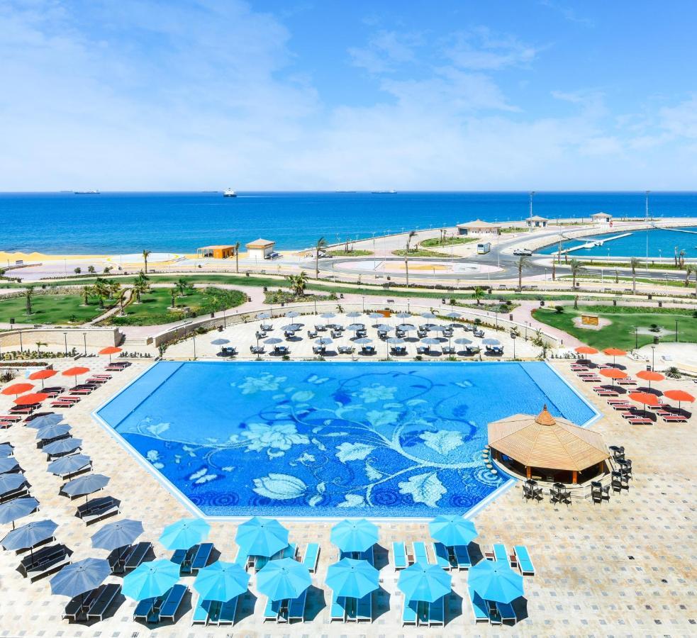 Tolip Resort El Galala Majestic Ain Sukhna Luaran gambar The photo features a large swimming pool with a decorative design on its surface, surrounded by sun loungers and umbrellas. In the background, there is a view of the sea, with a clear blue sky and a few scattered clouds. The area is well-maintained, 