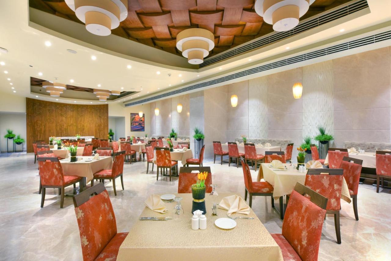 Tolip Resort El Galala Majestic Ain Sukhna Luaran gambar The photo shows the interior of a restaurant. The space features several tables set with light-colored tablecloths and chairs with reddish upholstery. Each table is adorned with decorative napkins and has small plants in the center. The room has a mo