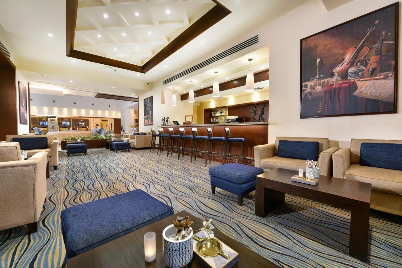 Tolip Resort El Galala Majestic Ain Sukhna Luaran gambar The photo depicts a modern, inviting lobby or lounge area. It features a cozy seating arrangement with light-colored sofas and deep blue accent chairs. In the center, there is a low wooden coffee table with decorative items, including a candle and sm