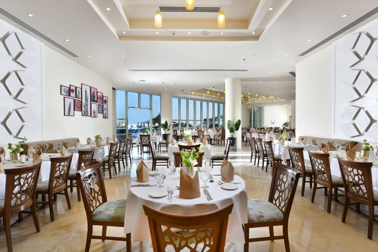 Tolip Resort El Galala Majestic Ain Sukhna Luaran gambar The photo displays a spacious and elegantly designed restaurant interior. It features numerous tables set for dining, with white tablecloths, neatly folded napkins, and decorative centerpieces of flowers. The seating consists of wooden chairs that co