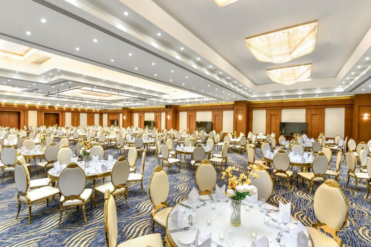 Tolip Resort El Galala Majestic Ain Sukhna Luaran gambar The photo shows a spacious and elegantly decorated banquet hall. The room features numerous round dining tables, each set with white tablecloths and adorned with decorative centerpieces, likely flowers. The chairs surrounding the tables have a luxuri